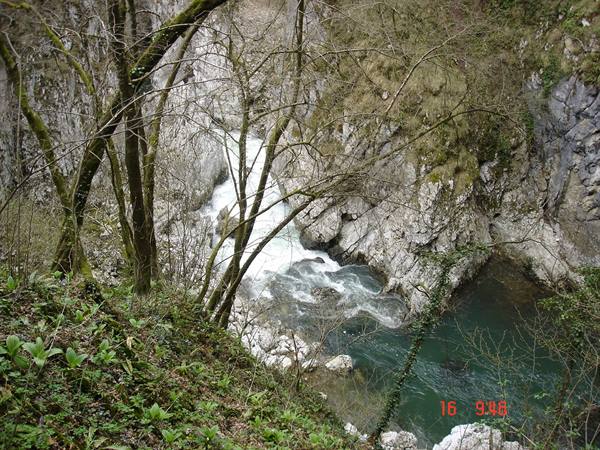Turquoise river rushing over rocks between limestone cliffs and bare trees
