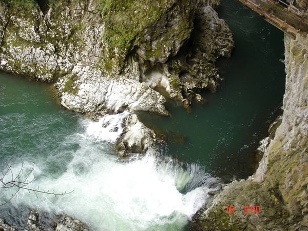 Turquoise river rushing over mossy rocks beneath a wooden bridge