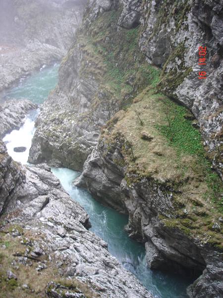 Turquoise river rushing between mossy rocky gorge walls in mist