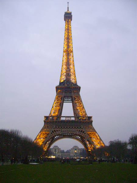 Eiffel Tower glowing golden at dusk, visitors on the lawn, Paris