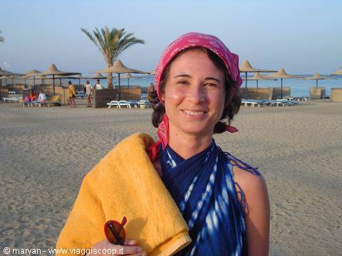 Smiling woman in red bandana and blue wrap on beach with umbrellas and palms