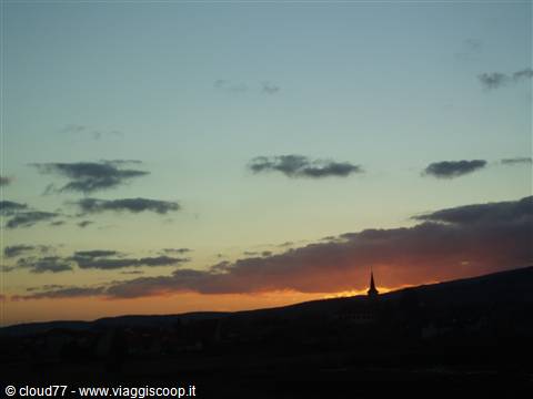Church spire silhouette on the hill, orange sky with dark clouds