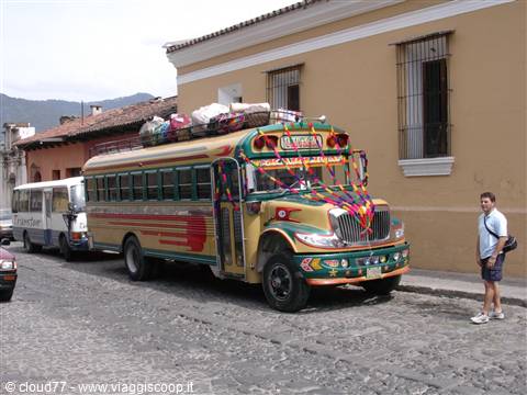 Colorful chicken bus loaded with luggage on cobblestone street, tourist nearby