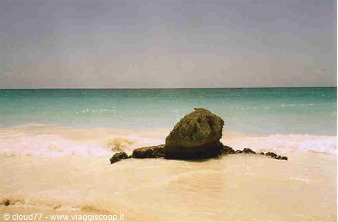 Dark rock on white sand beach, turquoise waves washing over it