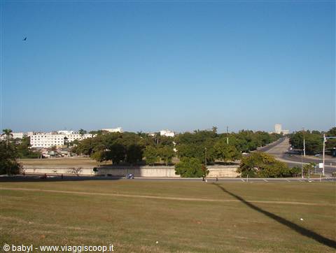 Green lawn before a stone fortress wall with palm trees, cars and buildings in background