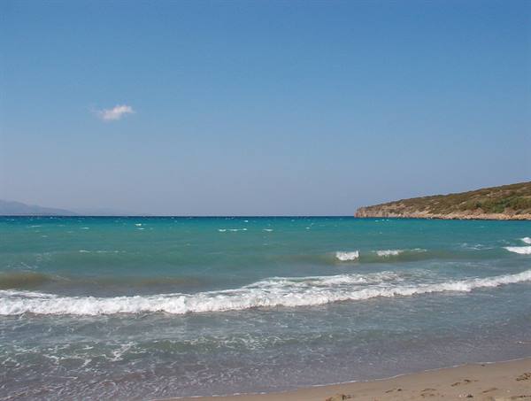 Turquoise waves on golden sand, green rocky coast to the right, clear sky