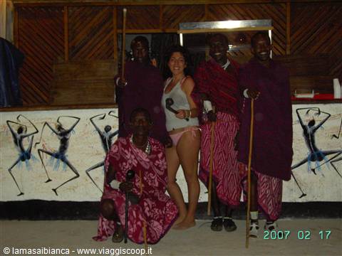 Tourist in swimsuit with Maasai men in red cloth by painted wall