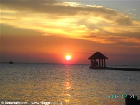 Low sun over the ocean, wooden pier with thatched hut backlit