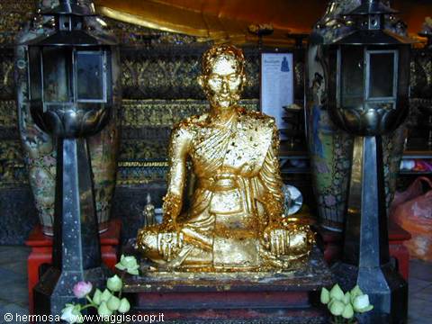Gold-leafed seated monk statue flanked by lanterns and lotus buds in a temple