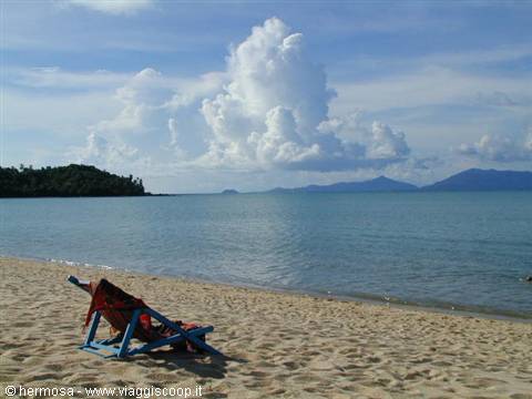 Empty deck chairs on the sand facing turquoise sea and islands