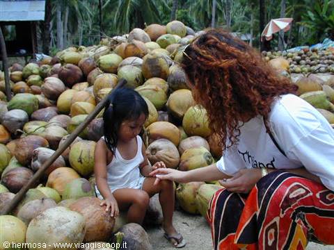 Woman leaning over girl sitting among coconut pile, natural daylight