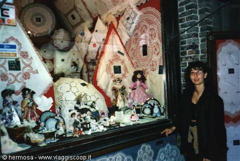 Woman beside a shop window displaying lace and dressed dolls