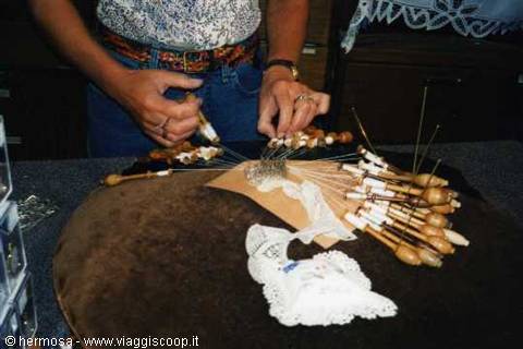 Craftswoman weaving wooden bobbins to make lace on a pillow