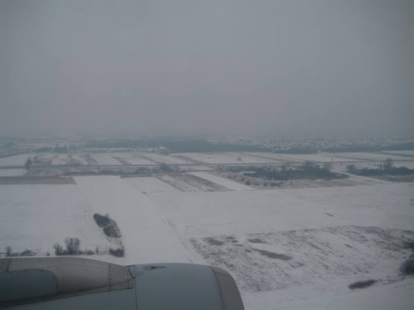Airplane wing over snowy fields in fog during landing