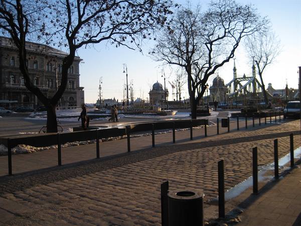 Cobbled square with bare trees, snow on the sides, Liberty Bridge at right
