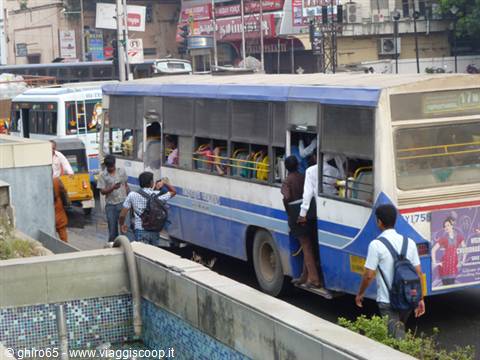Passengers board a blue and white bus stuck in city traffic
