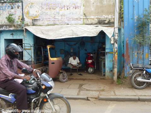 Motorcyclist passing a blue workshop where a man repairs a scooter