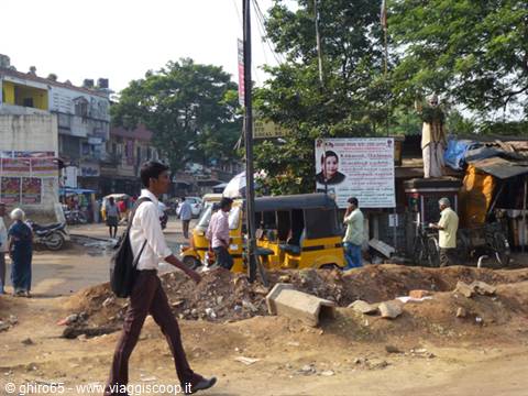 Man crosses sandy street among yellow auto-rickshaws, busy Indian town