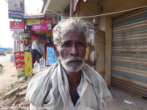 Elderly man with grey beard and light scarf in front of a shop with shutters