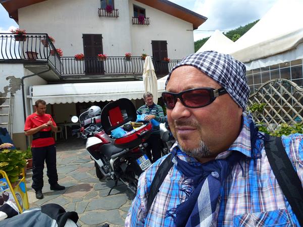 Motorcyclist with bandana and sunglasses in front of flowery balconies, loaded bikes