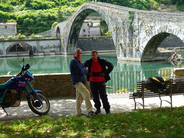 Two motorcyclists beside their bike beneath Ponte della Maddalena, Borgo a Mozzano