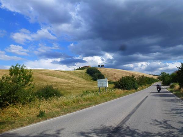 Motorcyclist on asphalt road among cultivated hills under cloudy sky
