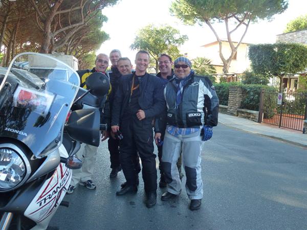 Five motorcyclists in riding gear beside a Honda Transalp on a tree-lined street