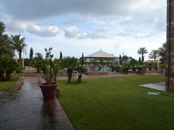 Pool with white gazebo among palms and wet lawn after rain