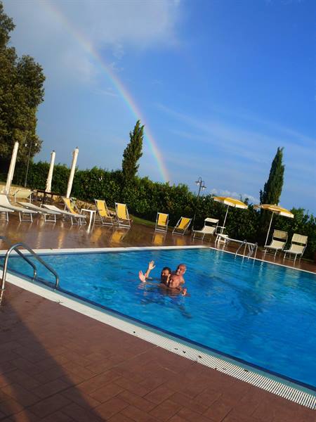 Two people swim in the pool with yellow umbrellas and a rainbow
