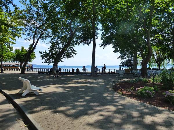 Tree-shaded lakeside promenade with brick paving and people by the railing