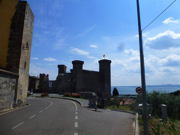Medieval stone fortress above the lake, road climbing up, blue sky