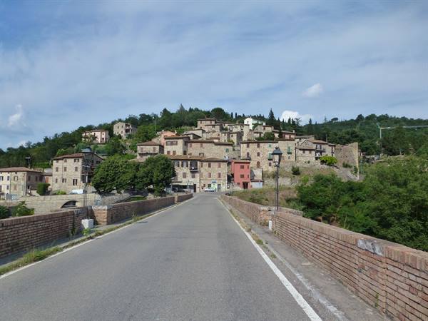 Road on brick bridge leading to stone medieval village on the hillside
