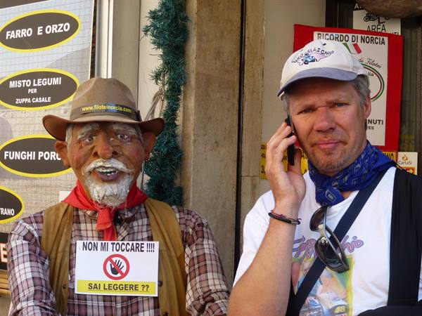 Tourist on phone beside a fake shepherd figure in Norcia shop display