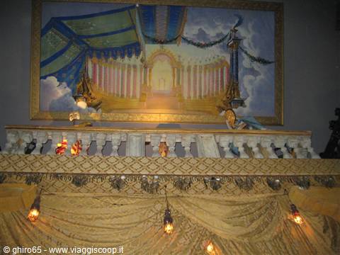 Stage with painted backdrop, marble balustrade and golden draped curtains lit by lamps