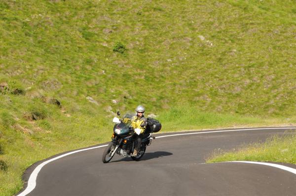 Motorcyclist with helmet leaning into asphalt curve among green grassy slopes