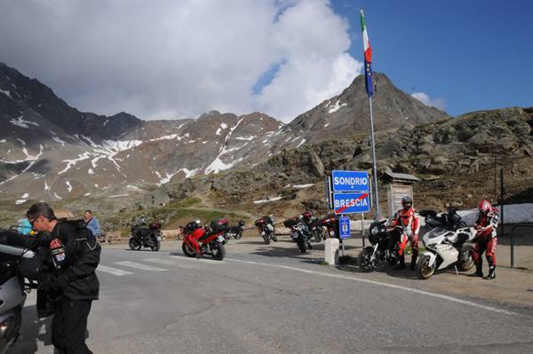 Motorcyclists stopped at Gavia Pass, Sondrio-Brescia sign, rocky snowy mountains