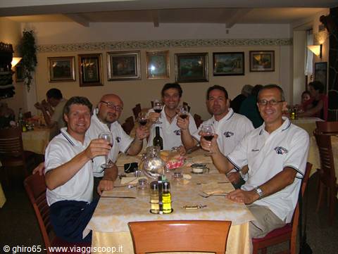 Five friends raising red wine glasses in a trattoria with paintings on walls