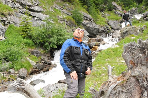 Motorcyclist in blue jacket beside a mountain stream among rocks