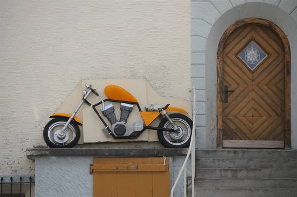 Orange and black motorcycle propped against a wall beside a wooden door