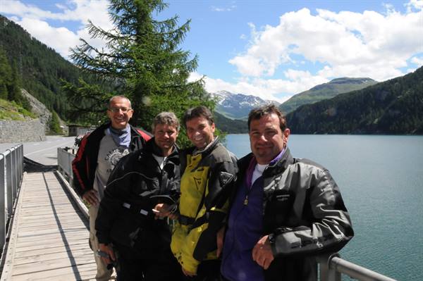 Four motorcyclists on the dam walkway beside the alpine reservoir