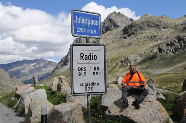 Man sitting on a rock next to the Julierpass 2284 m sign