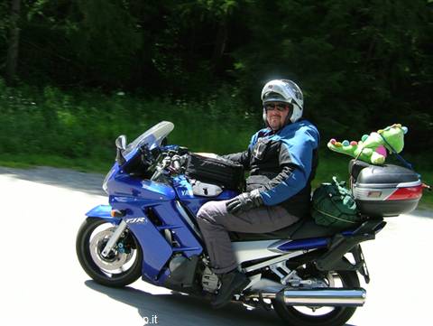 Motorcyclist in white helmet on blue touring bike, plush toy, forest road