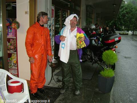 Two motorcyclists in rain suits standing outside a shop in the rain