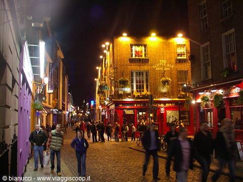 Crowds walking at night past illuminated Temple Bar pubs in Dublin