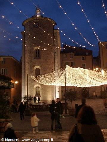 Illuminated medieval tower on a square with festive string lights and people
