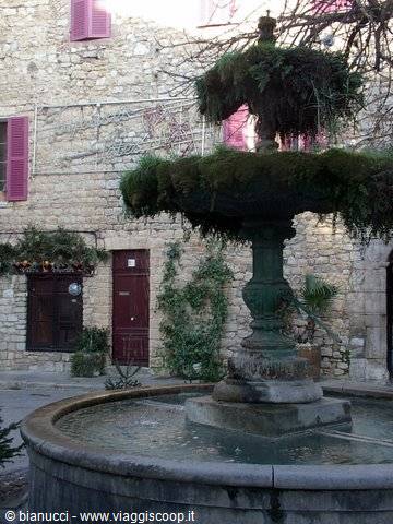 Moss-covered stone fountain in front of old houses with pink shutters