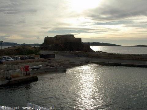 Old coastal fortress seen from the harbor, sunlight reflecting on the sea