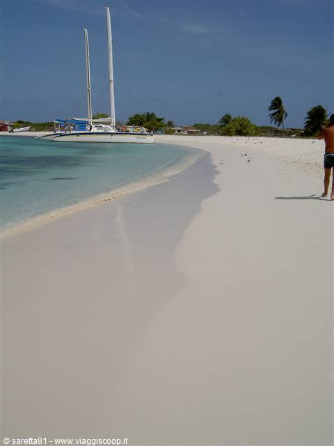Catamaran moored near white sand beach, turquoise water, man walking