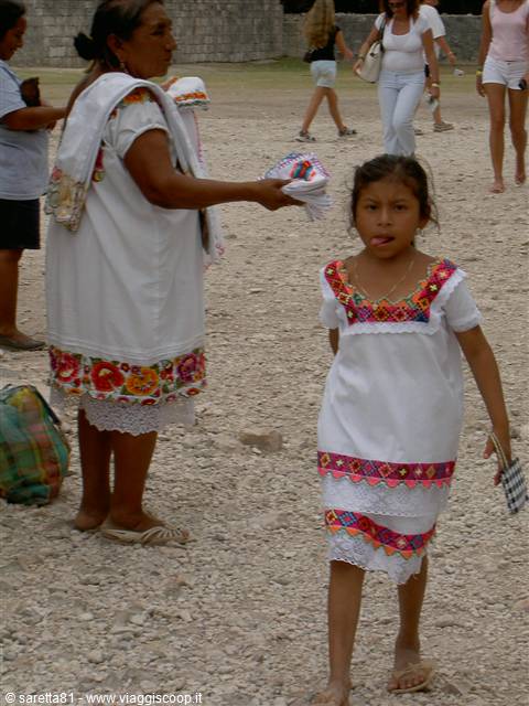 Girl and woman in embroidered Maya dresses sell souvenirs near stone ruins