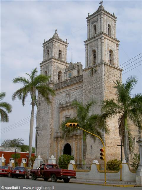 Colonial stone church with two bell towers, palm trees and parked red pickup